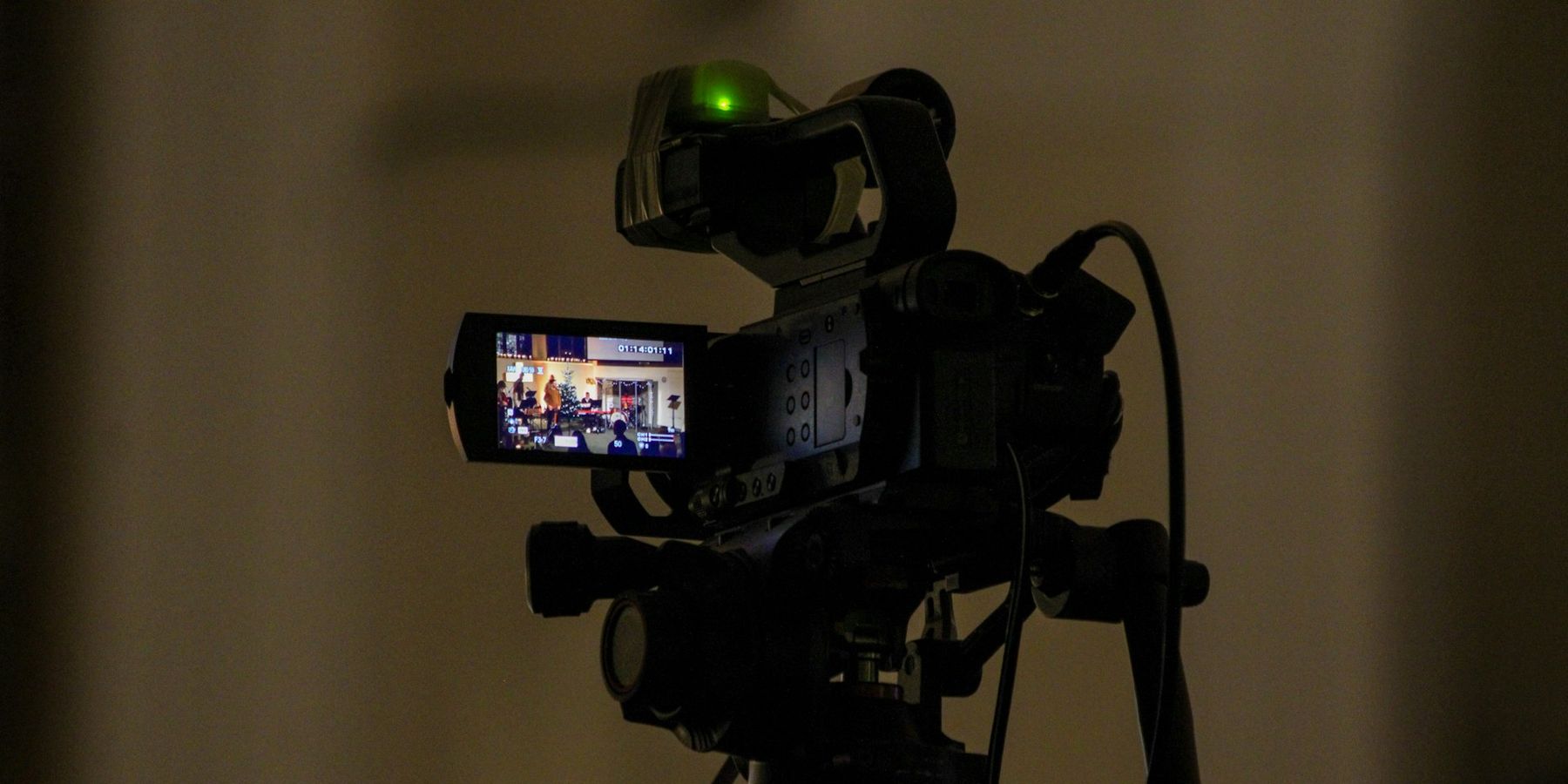 A professional video camera on a tripod with its record light on